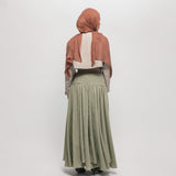 Woman wearing a hijab, light-colored top, and green skirt on a white background
