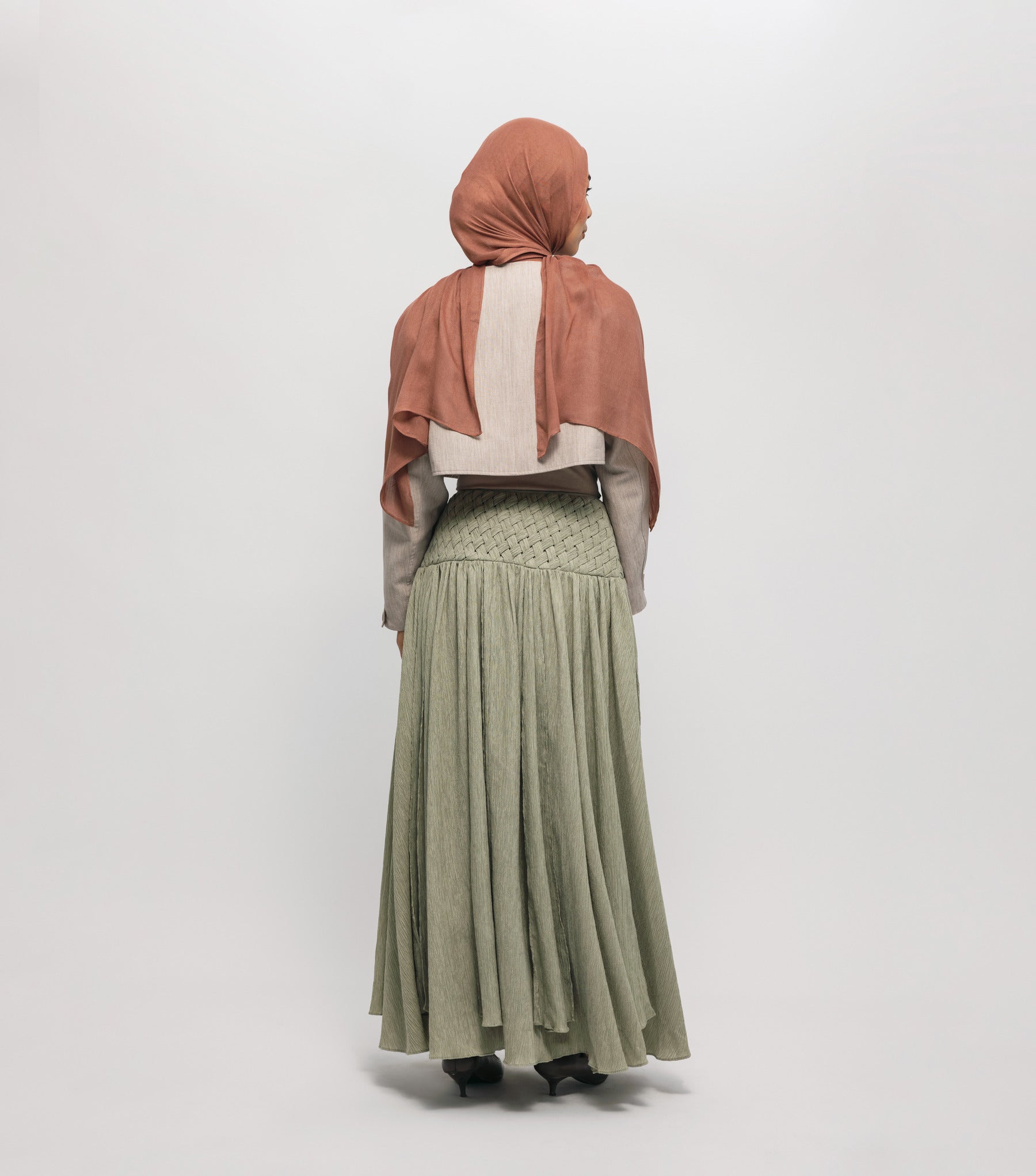 Woman wearing a hijab, light-colored top, and green skirt on a white background