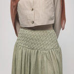 Woman wearing a hijab, light-colored top, and green skirt on a white background
