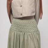 Woman wearing a hijab, light-colored top, and green skirt on a white background