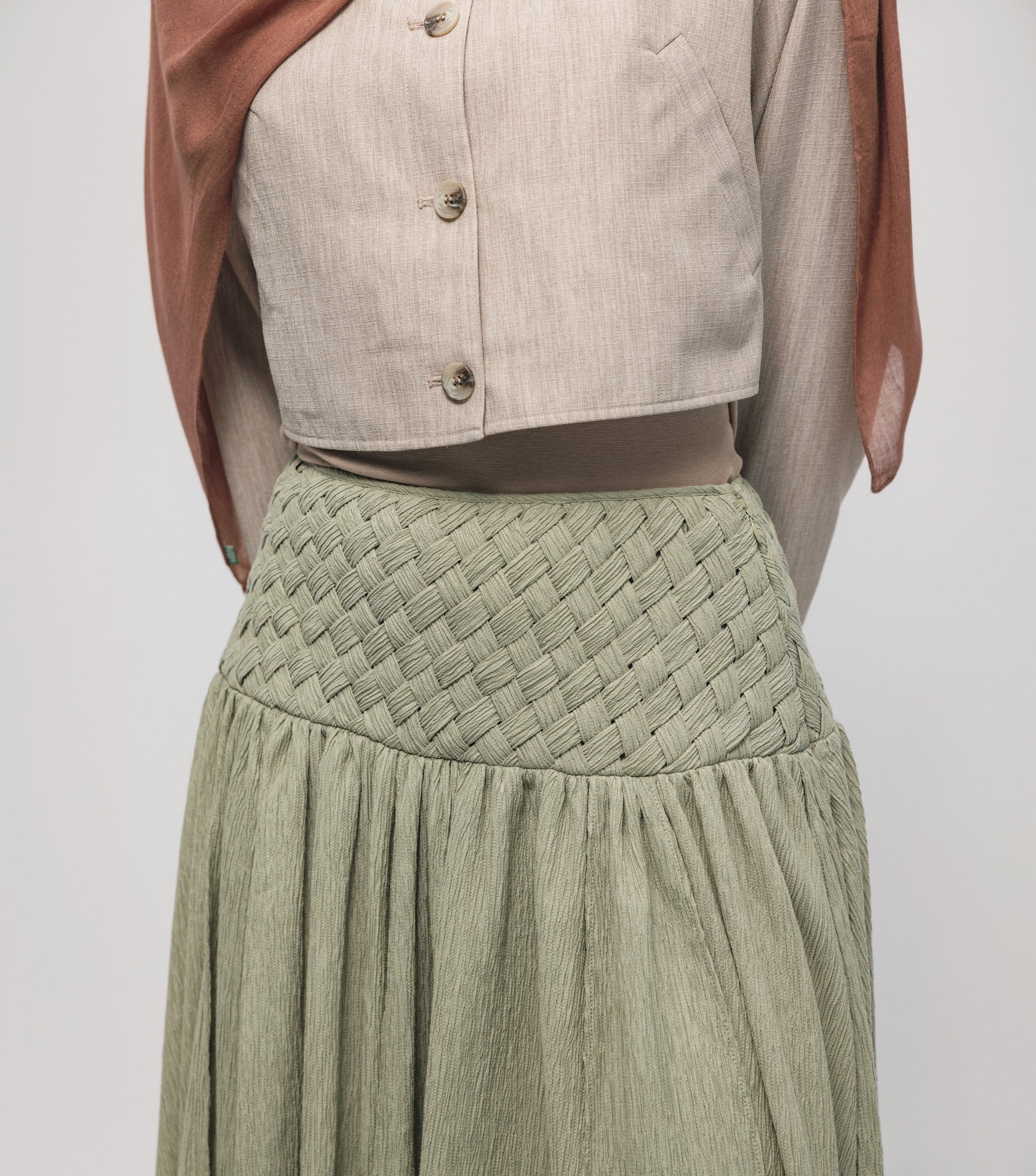 Woman wearing a hijab, light-colored top, and green skirt on a white background