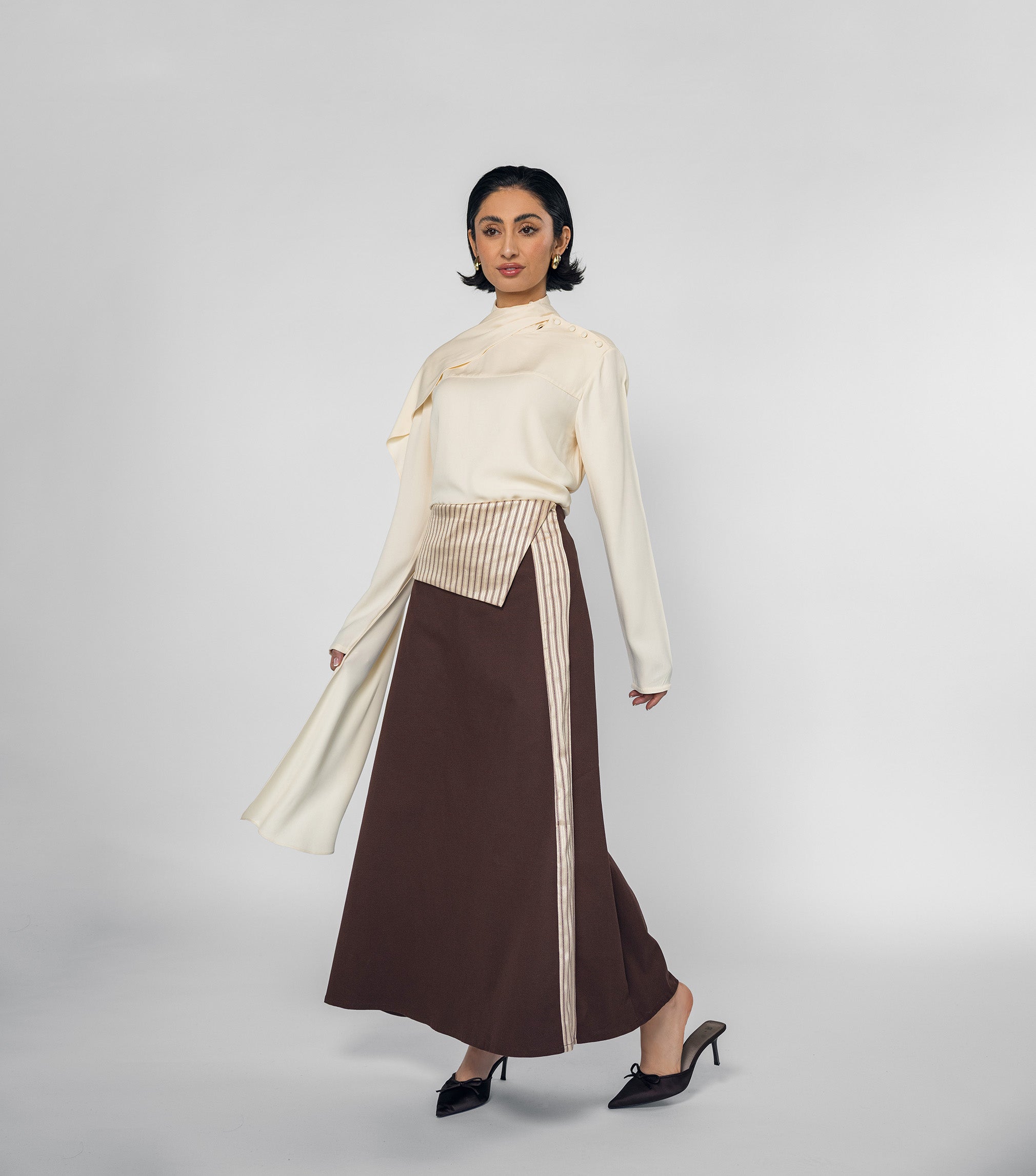 Woman wearing a cream blouse and brown skirt with a white background
