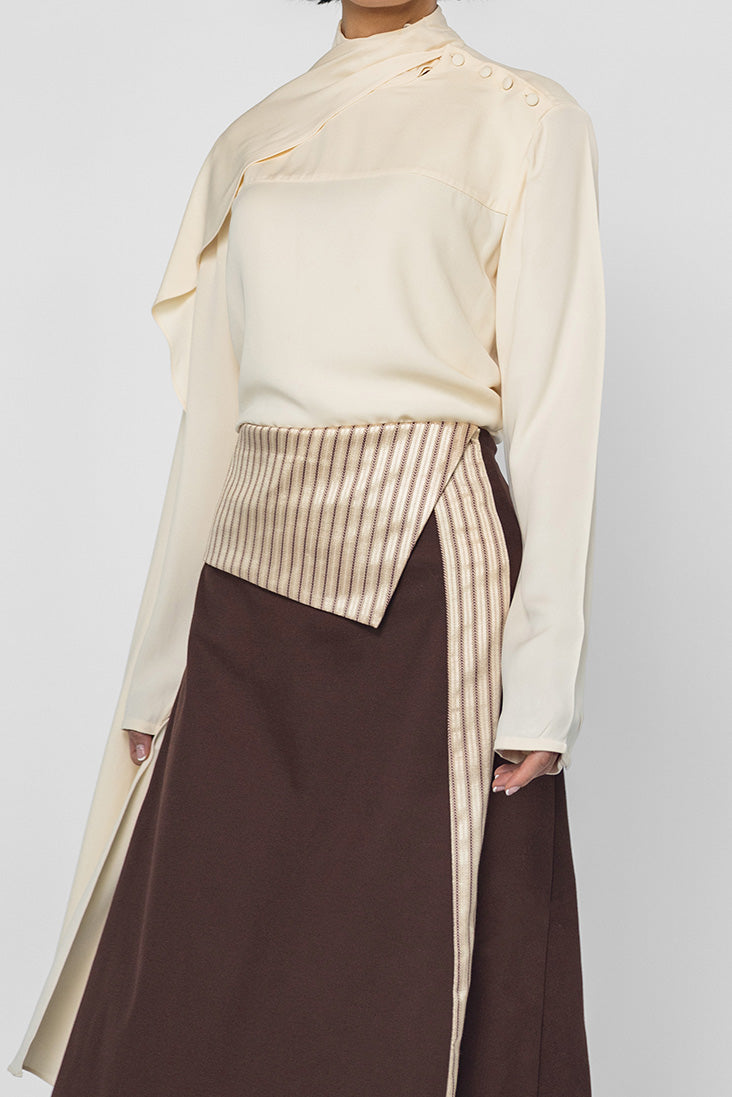 Person wearing a cream blouse with a high collar and a brown skirt on a white background