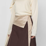 Person wearing a cream blouse with a high collar and a brown skirt on a white background