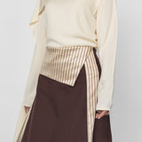 Person wearing a cream blouse with a high collar and a brown skirt on a white background