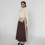 Woman wearing a cream top and brown skirt with a striped detail on a white background