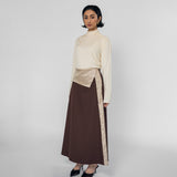 Woman wearing a cream top and brown skirt with a striped detail on a white background