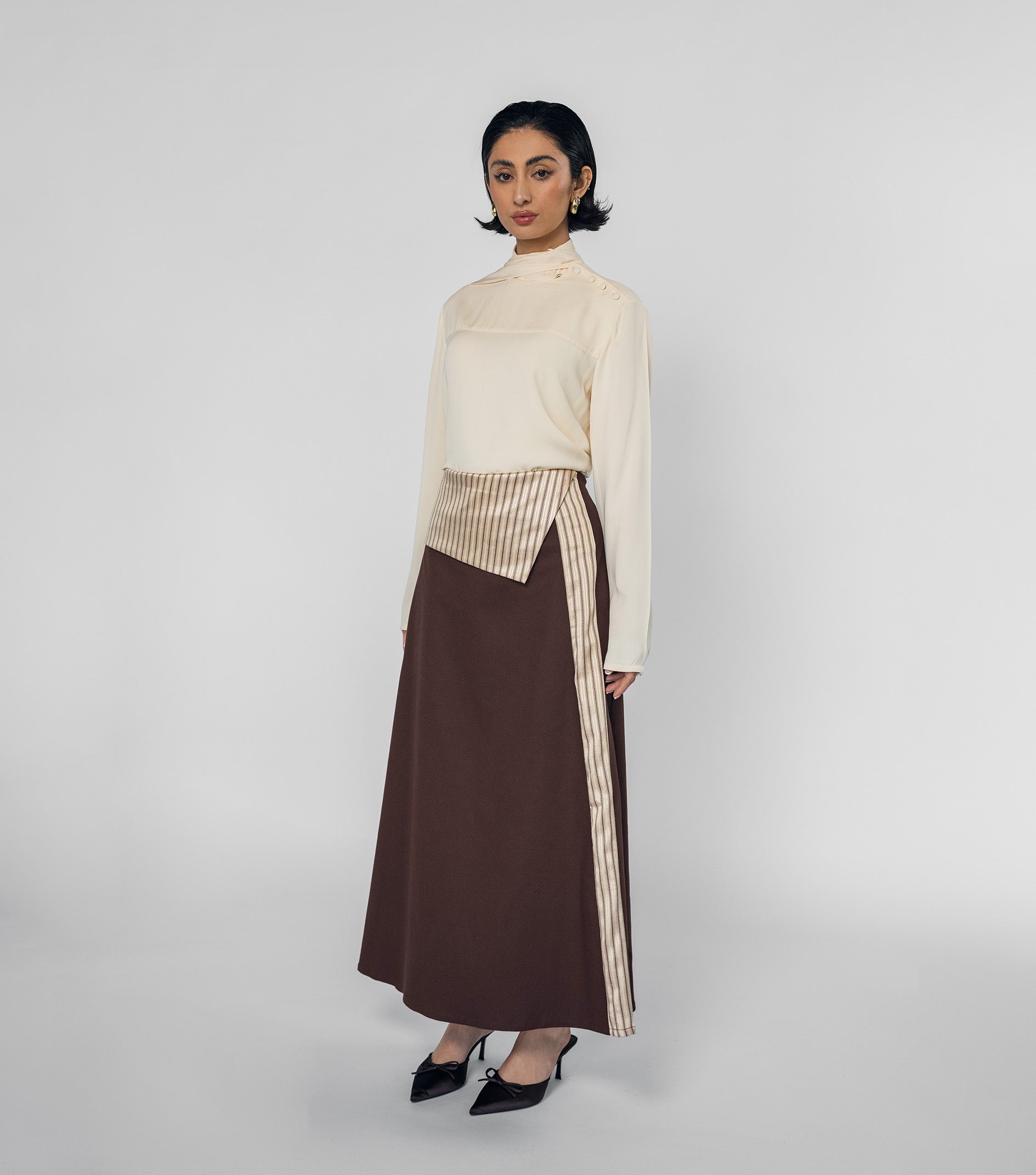 Woman wearing a cream top and brown skirt with a striped detail on a white background
