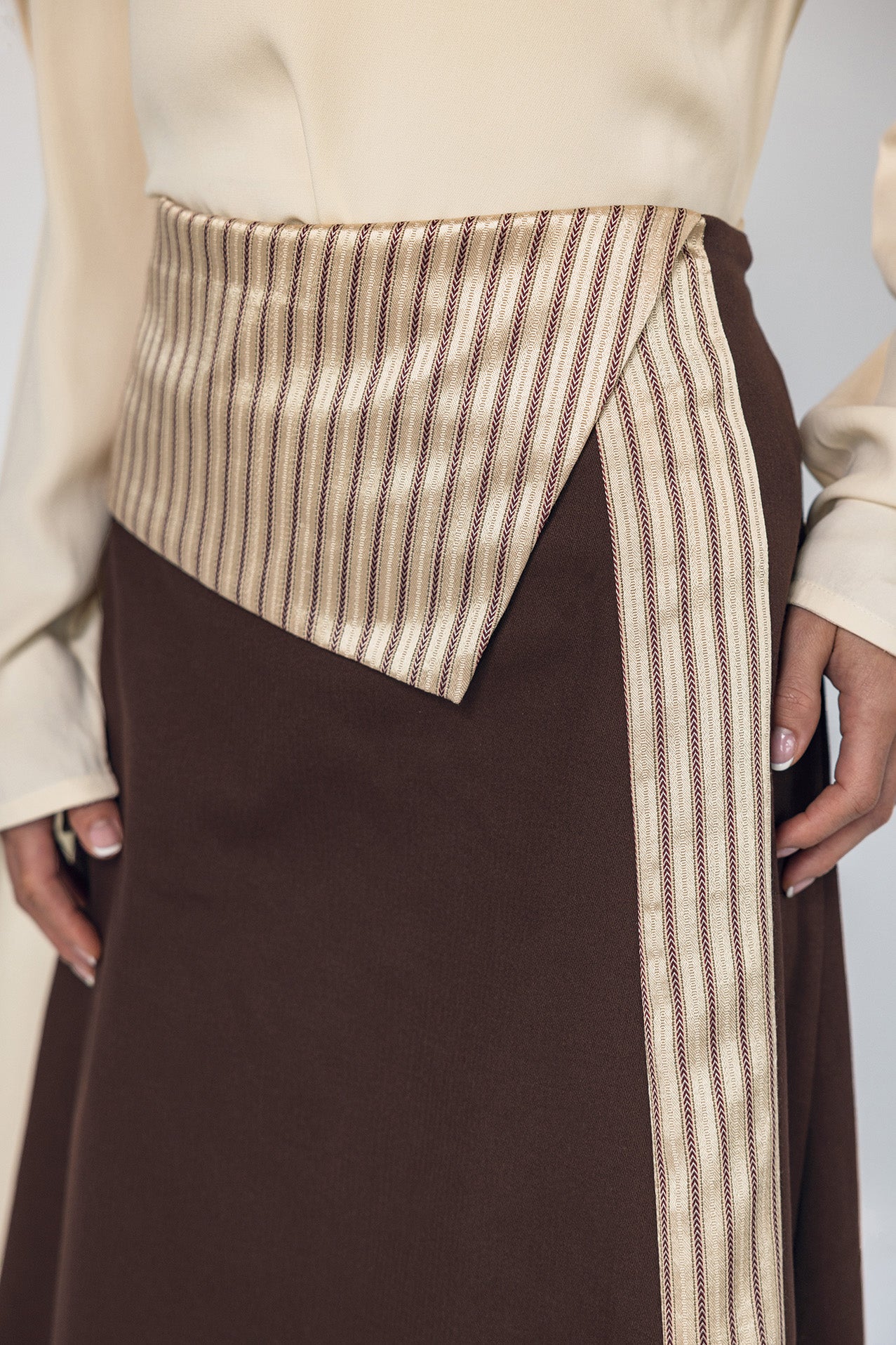 Brown skirt with a striped detail worn by a person on a plain background