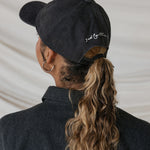 Person wearing a black cap with text, facing away from the camera.