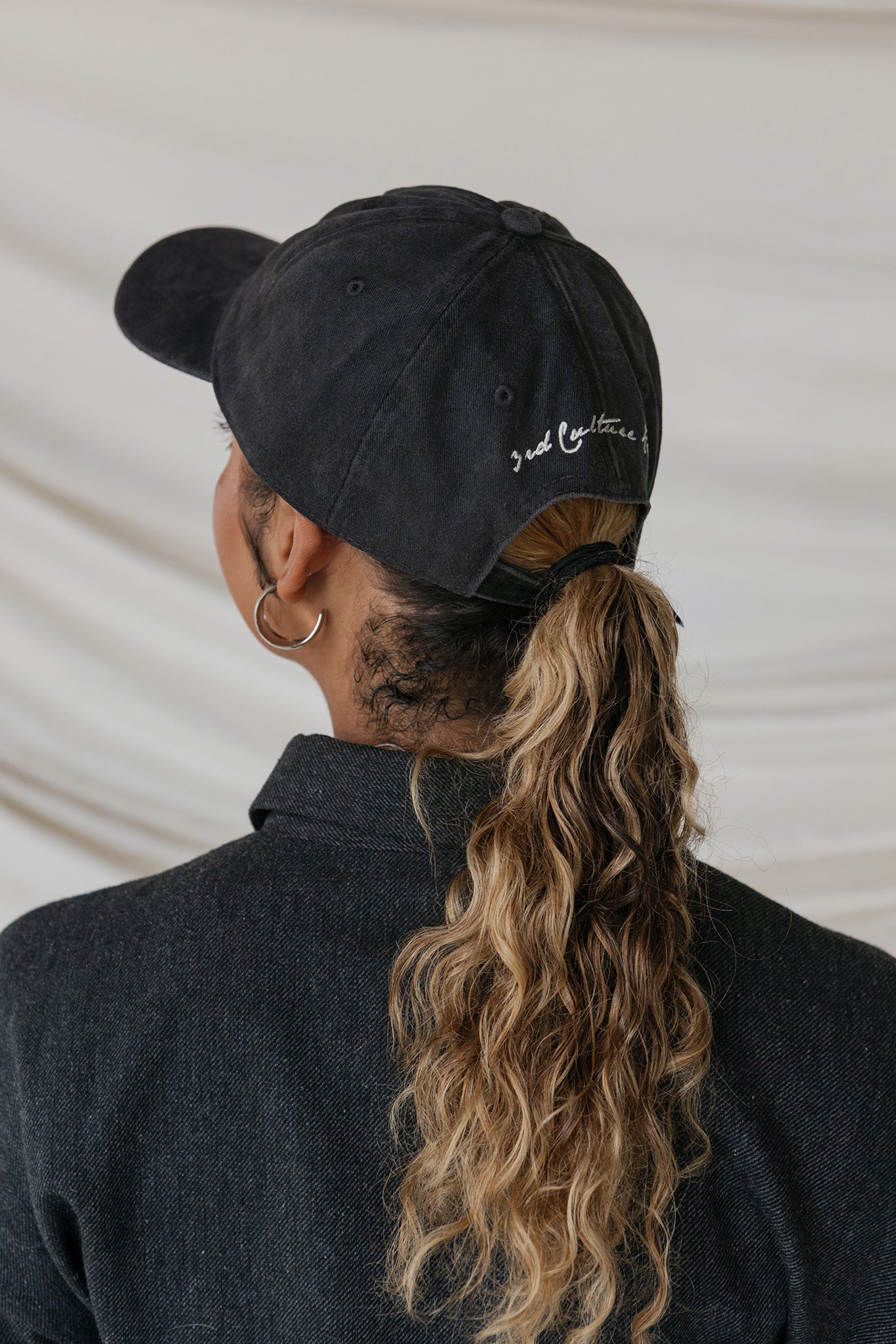 Person wearing a black cap with text, facing away from the camera.