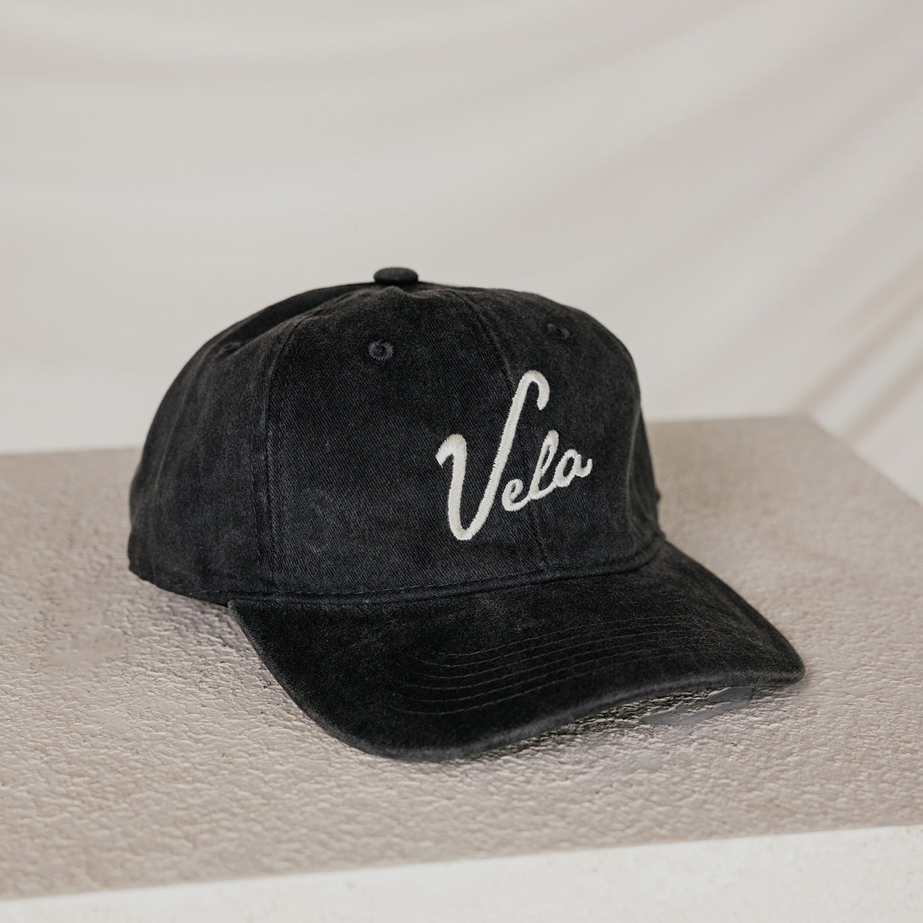 Black cap with 'Vela' logo on a neutral background