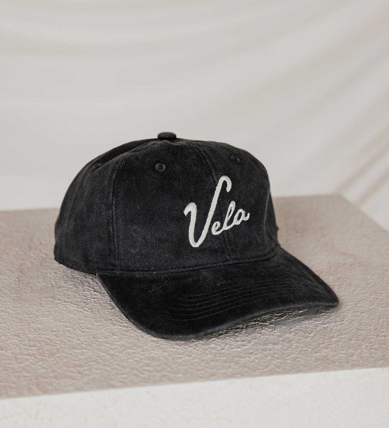 Black cap with 'Vela' logo on a neutral background