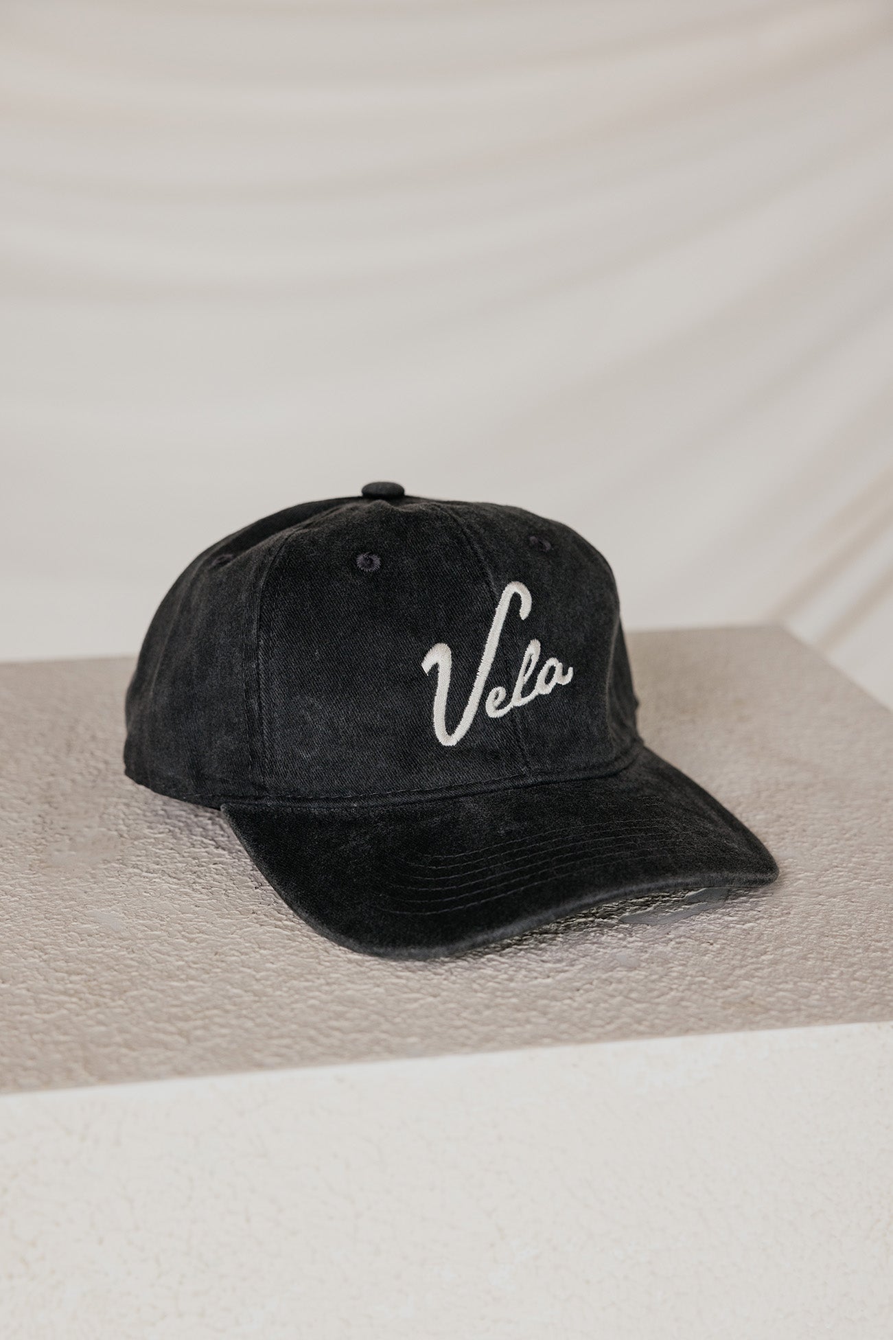 Black cap with 'Vela' logo on a neutral background