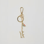 Gold keychain with 'VELA' initials and watermelon charm on a light gray background.