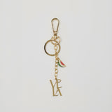 Gold keychain with 'VELA' initials and watermelon charm on a light gray background.