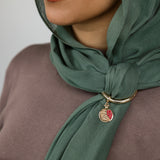 Woman wearing a green hijab with a gold hoop and pomegranate charm.