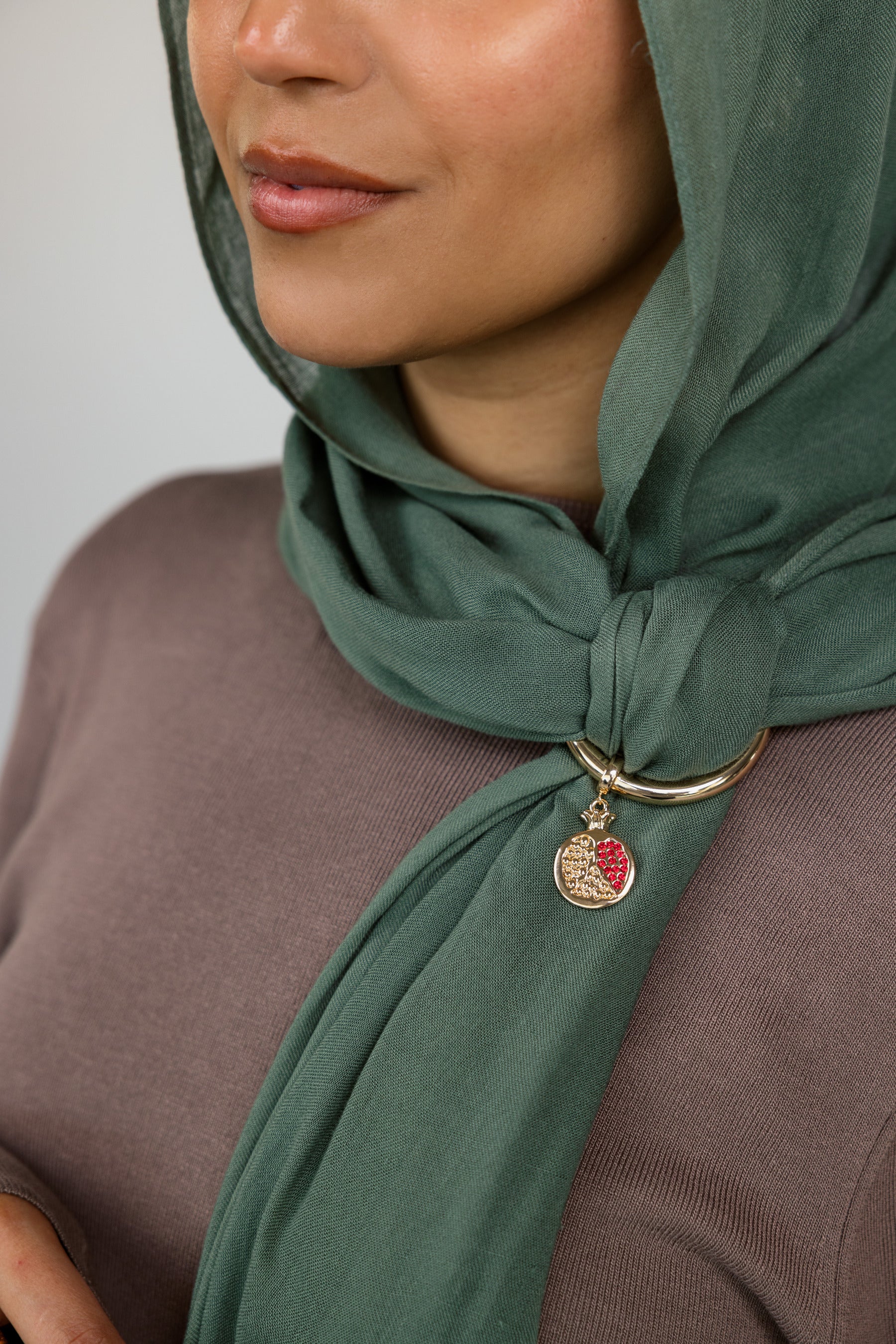 Woman wearing a green hijab with a gold hoop and pomegranate charm.