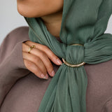 Person wearing a green hijab with a gold hijab hoop, against a neutral background.