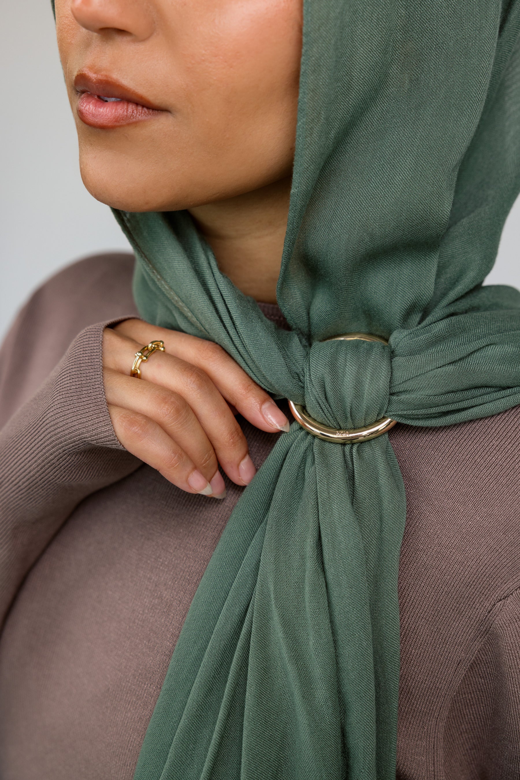 Person wearing a green hijab with a gold hijab hoop, against a neutral background.