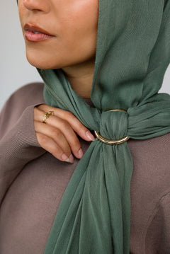 Person wearing a green hijab with a gold hijab hoop, against a neutral background.