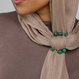 Close-up of a beige hijab with emerald green hoop on a neutral background.