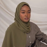 Woman wearing a green chiffon hijab and brown outfit against a plain background