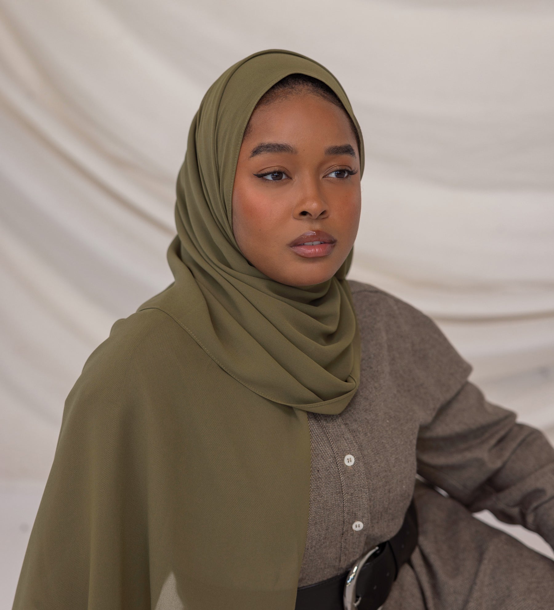 Woman wearing a green chiffon hijab and brown outfit against a plain background