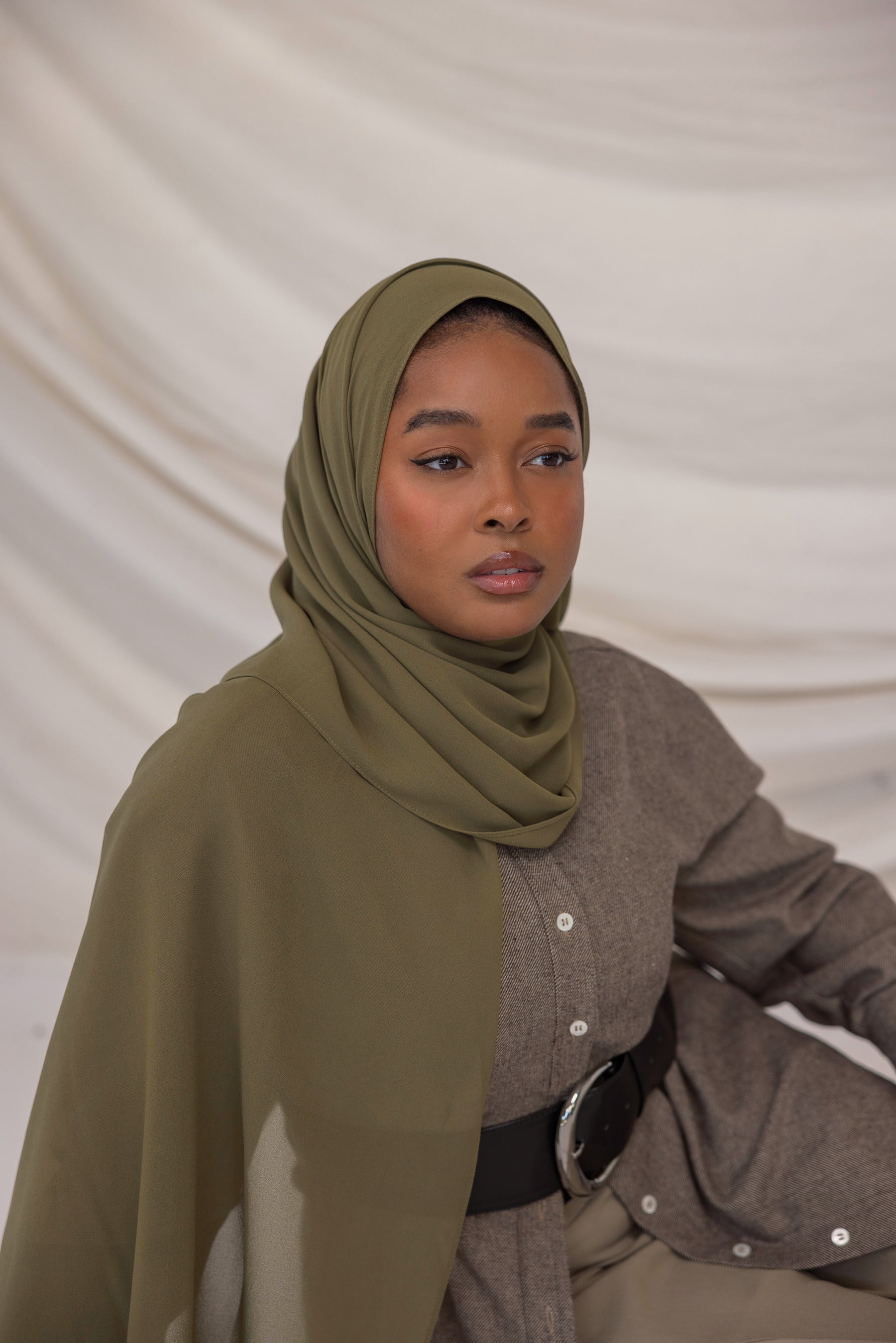 Woman wearing a green chiffon hijab and brown outfit against a plain background