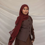 Woman wearing a brown outfit with a red chiffon hijab against a beige background