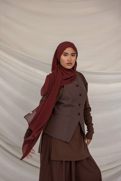 Woman wearing a brown outfit with a red chiffon hijab against a beige background