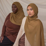 Two women wearing brown chiffon hijabs against a plain background