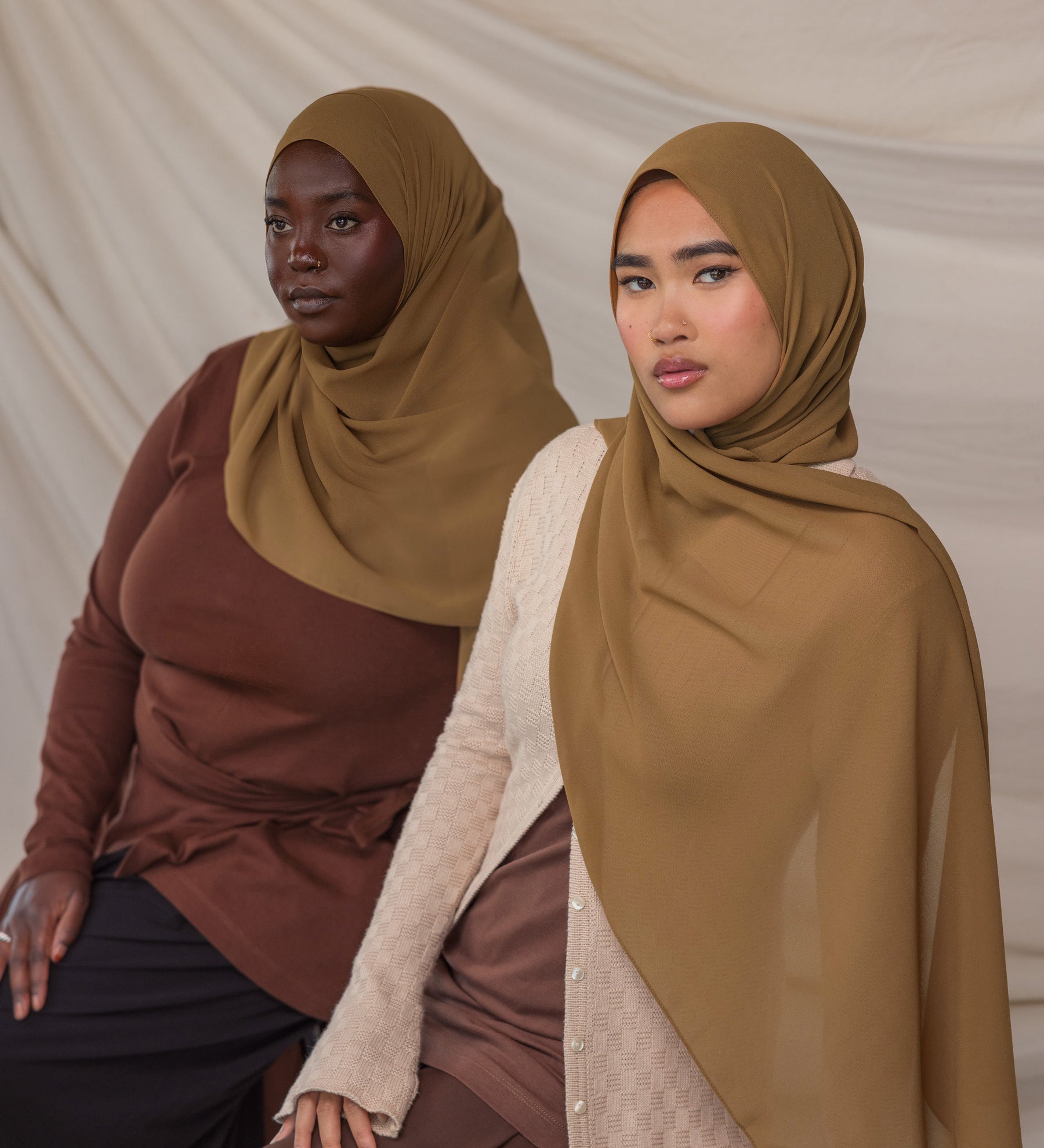 Two women wearing brown chiffon hijabs against a plain background