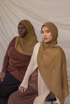 Two women wearing brown chiffon hijabs against a plain background