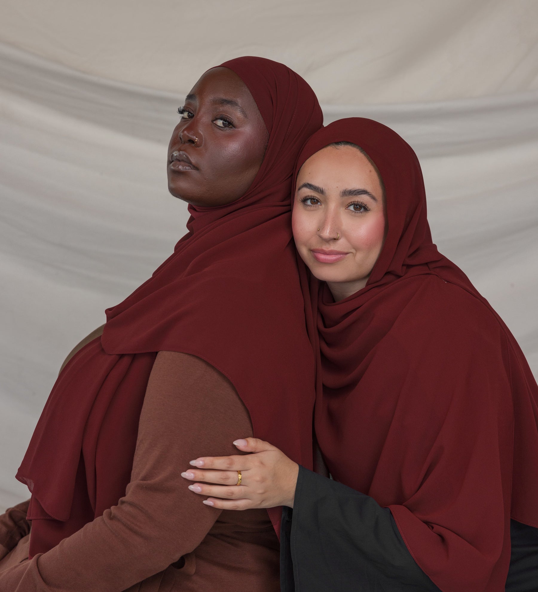 Two women wearing maroon hijabs against a plain background