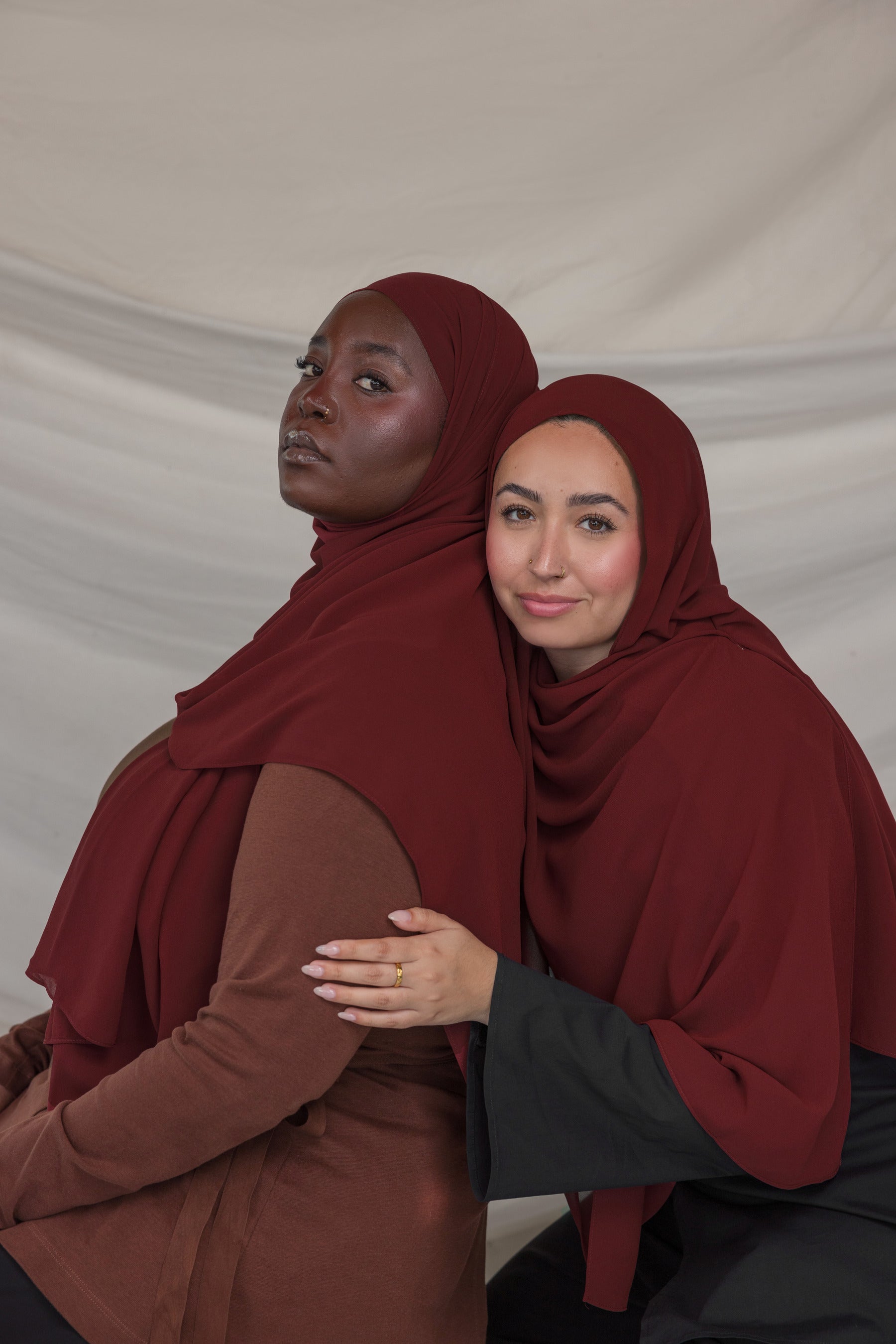 Two women wearing maroon hijabs against a plain background