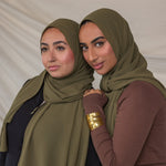 Two women wearing green chiffon hijabs posing against a plain background