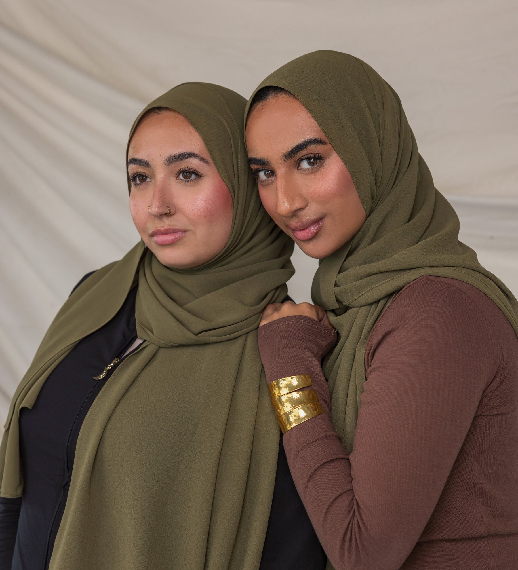 Two women wearing green chiffon hijabs posing against a plain background