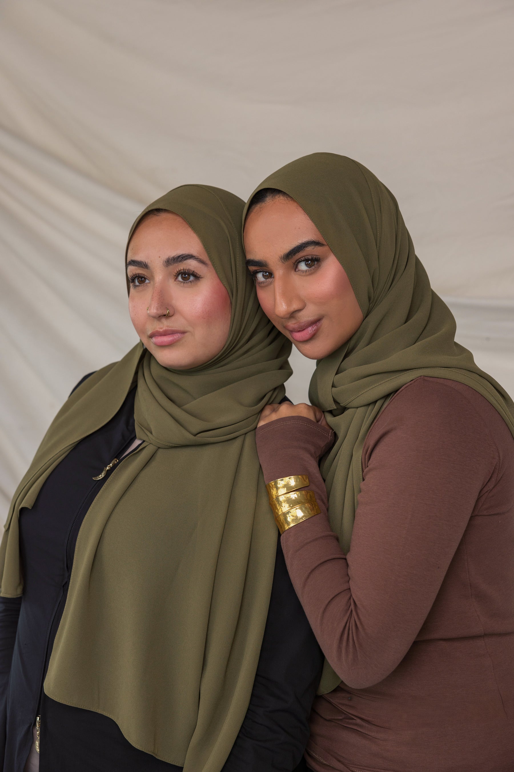 Two women wearing green chiffon hijabs posing against a plain background