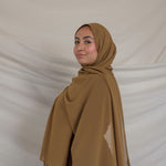 Woman wearing a brown chiffon hijab and outfit against a plain background
