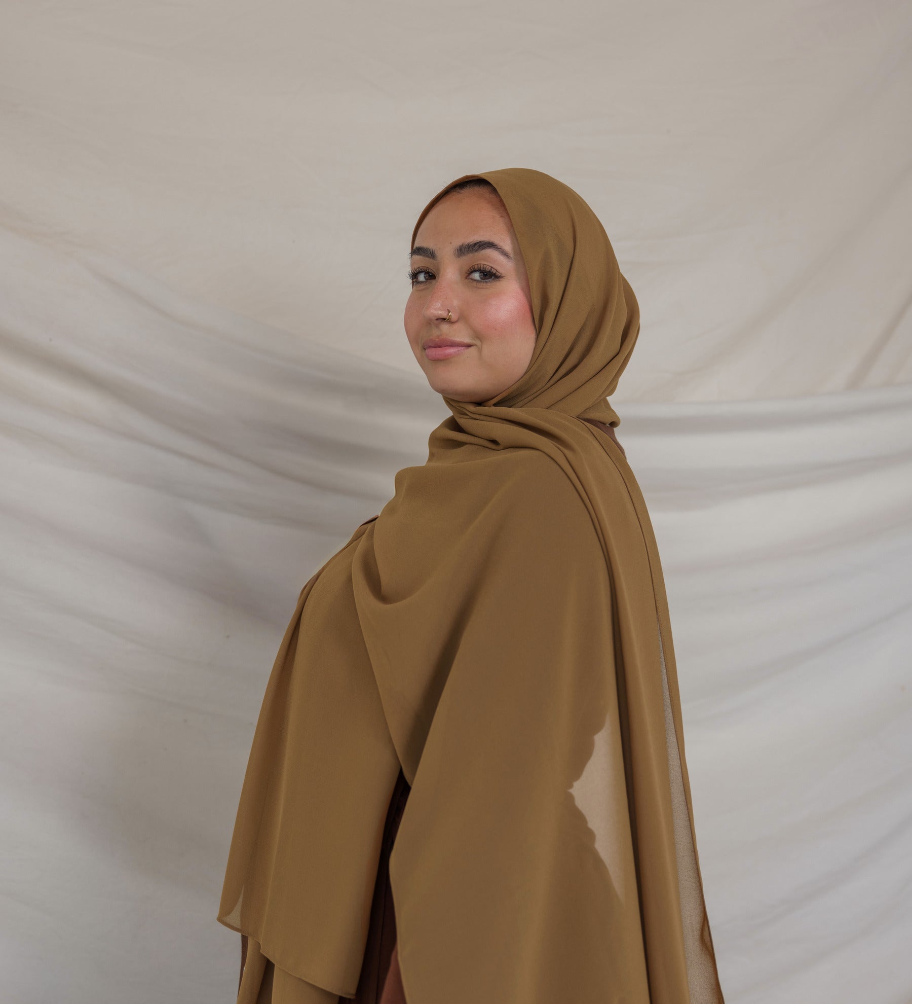 Woman wearing a brown chiffon hijab and outfit against a plain background