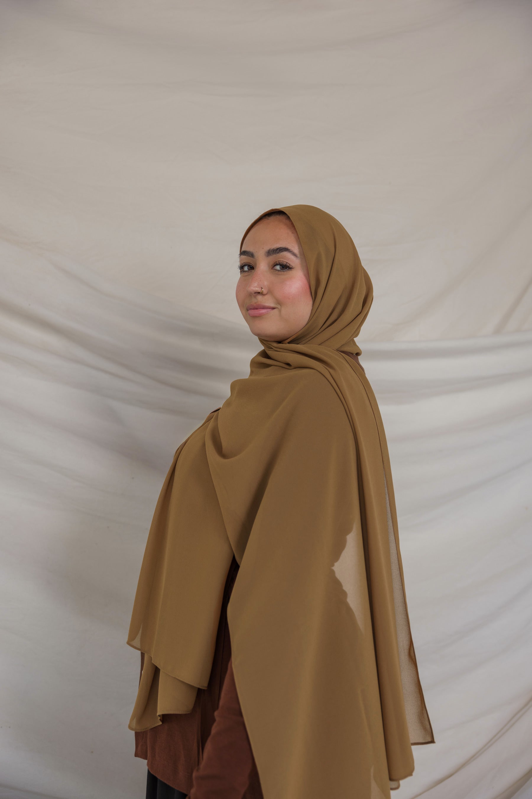 Woman wearing a brown chiffon hijab and outfit against a plain background