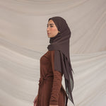 Woman wearing a brown hijab and dress against a beige background