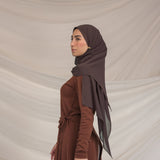 Woman wearing a brown hijab and dress against a beige background