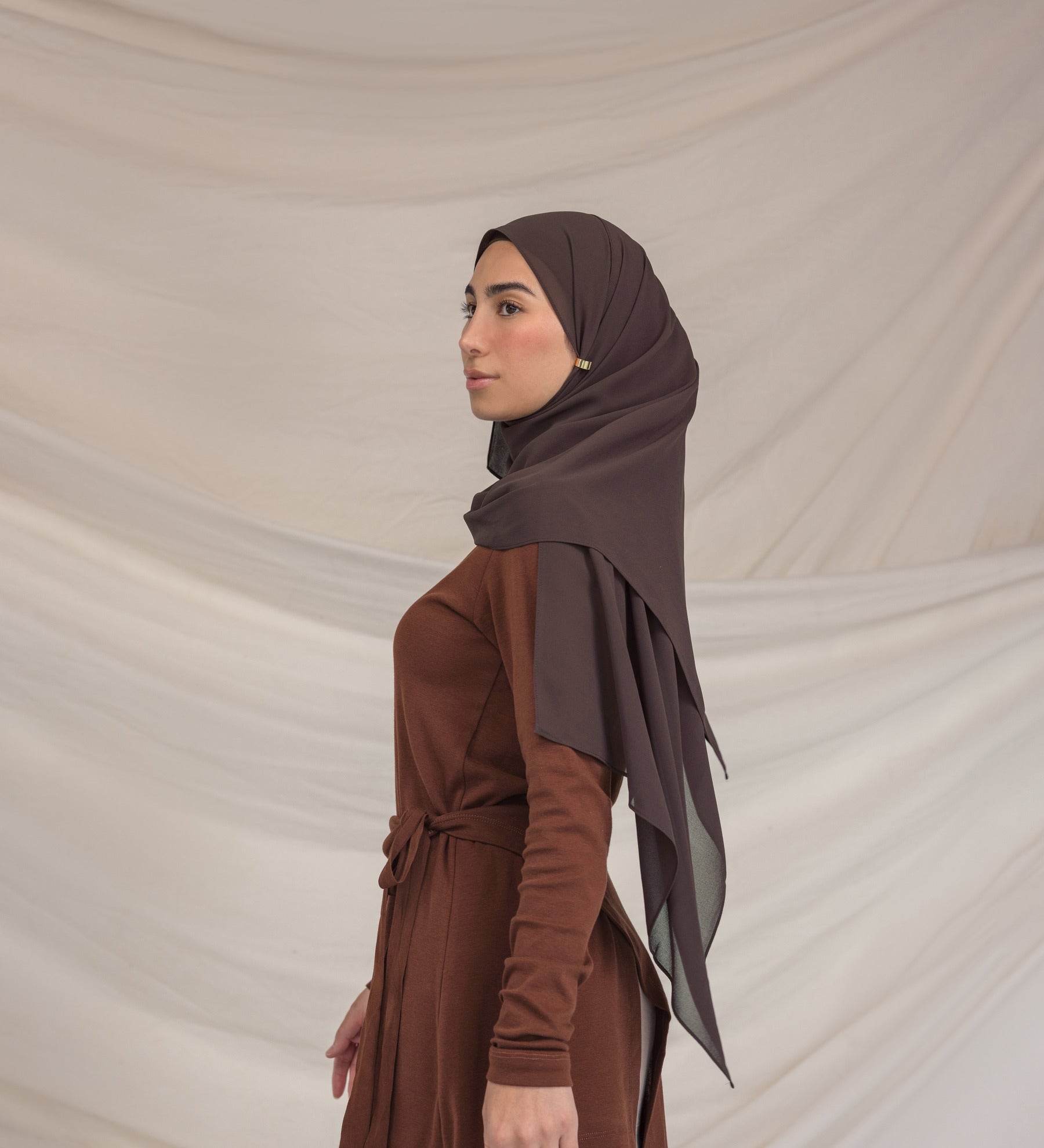 Woman wearing a brown hijab and dress against a beige background
