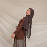 Woman wearing a brown outfit with a brown chiffon hijab against a beige background
