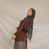 Woman wearing a brown outfit with a brown chiffon hijab against a beige background