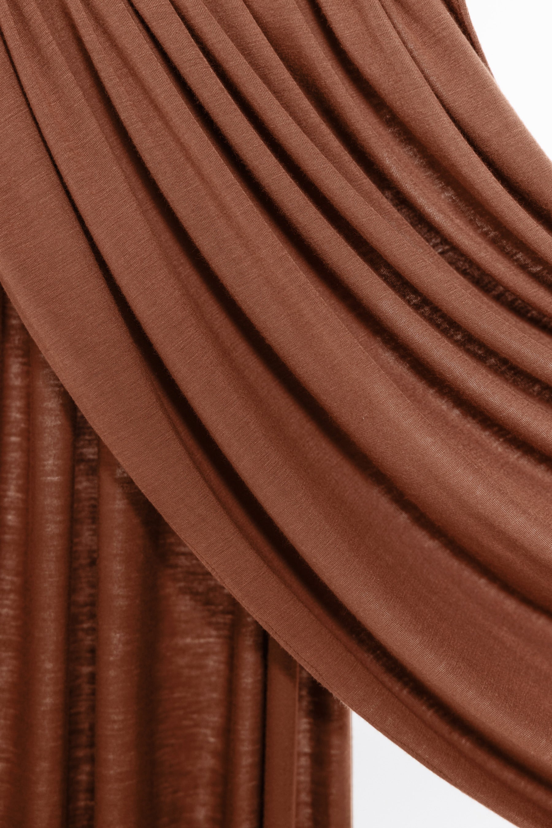 Close-up of draped brown fabric with soft folds and a slightly textured surface, shown against a small white background.