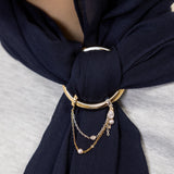 A close-up of a navy blue scarf tied around the neck of a person, secured with a gold-toned ring and layered chain accessory.