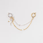 A delicate double-layered chain earring accessory featuring a gold chain with a small pearl bead and a silver chain with a clear rhinestone, attached to a gold and silver hoop earring on a light gray background.